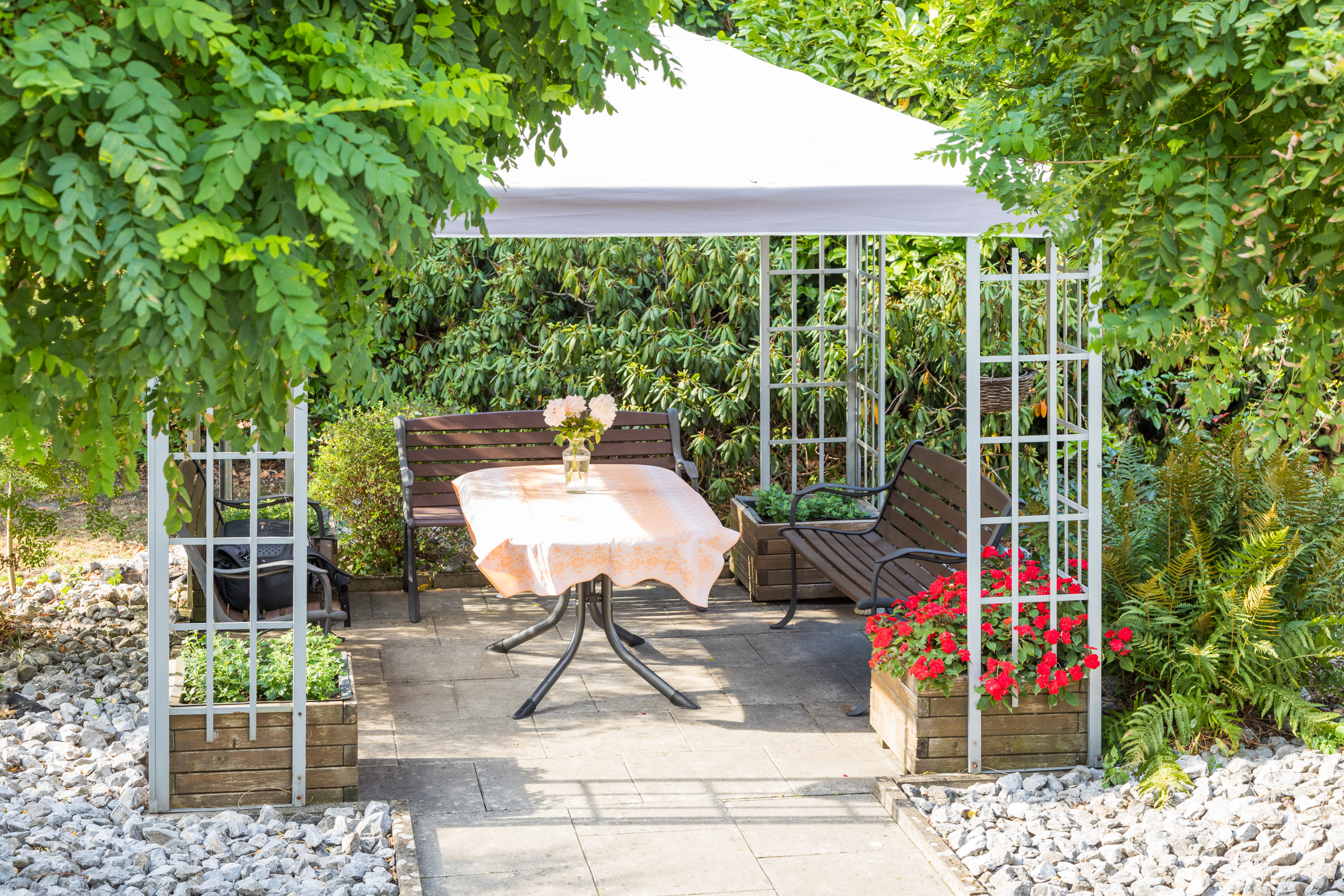 Überdachter Sitzbereich im Garten mit Bank und gedecktem Tisch