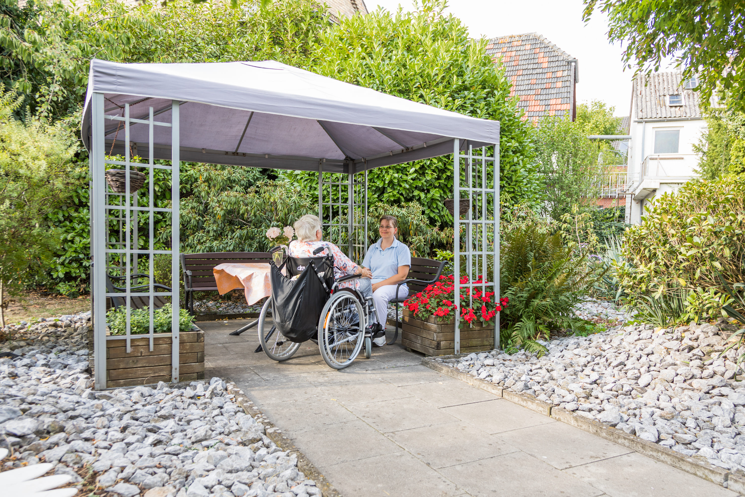 Pflegekraft im Gespräch mit einer Bewohnerin im Rollstuhl im Gartenpavillon