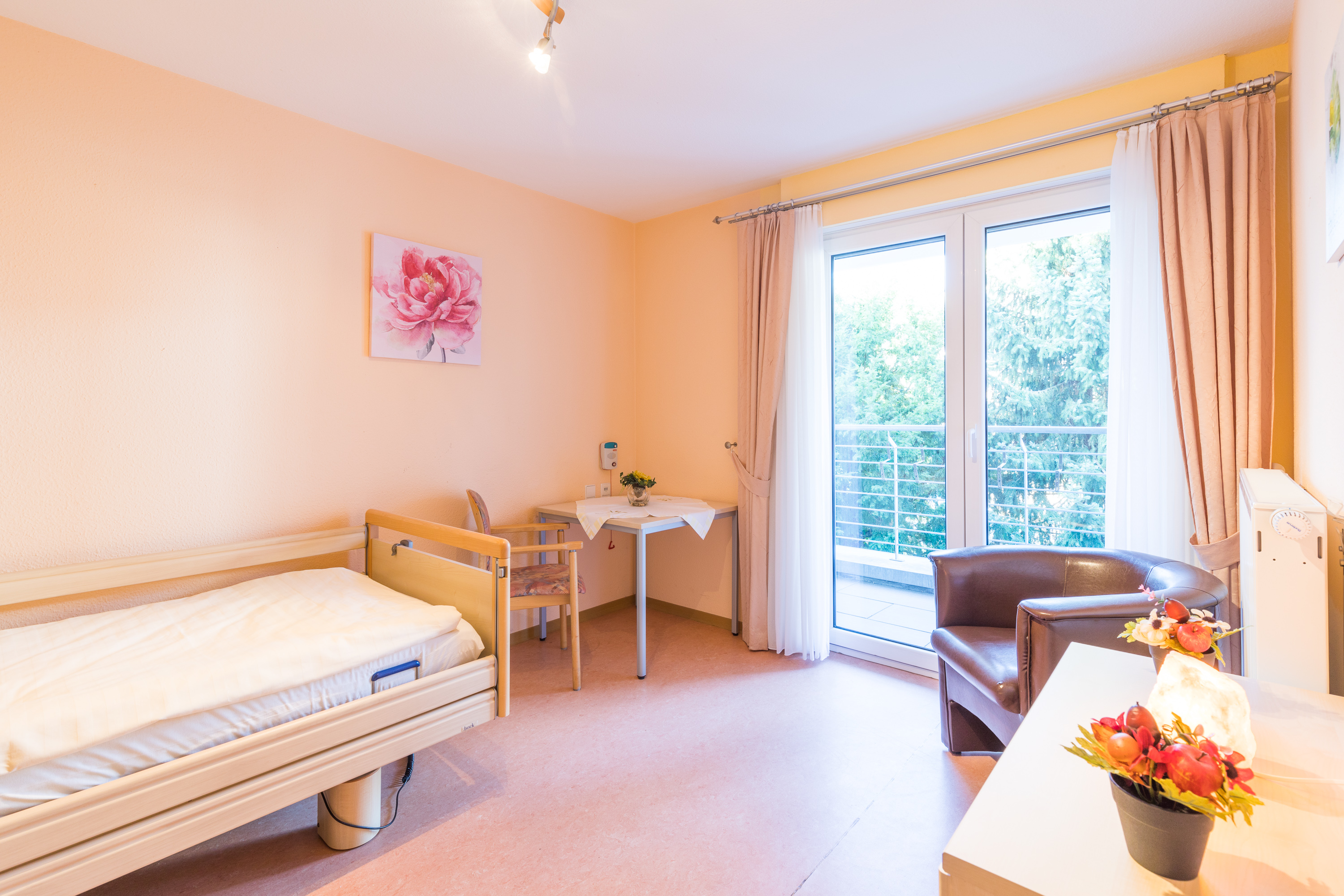 Pflegezimmer mit Pflegebett, Sitzecke und Zugang zum Balkon